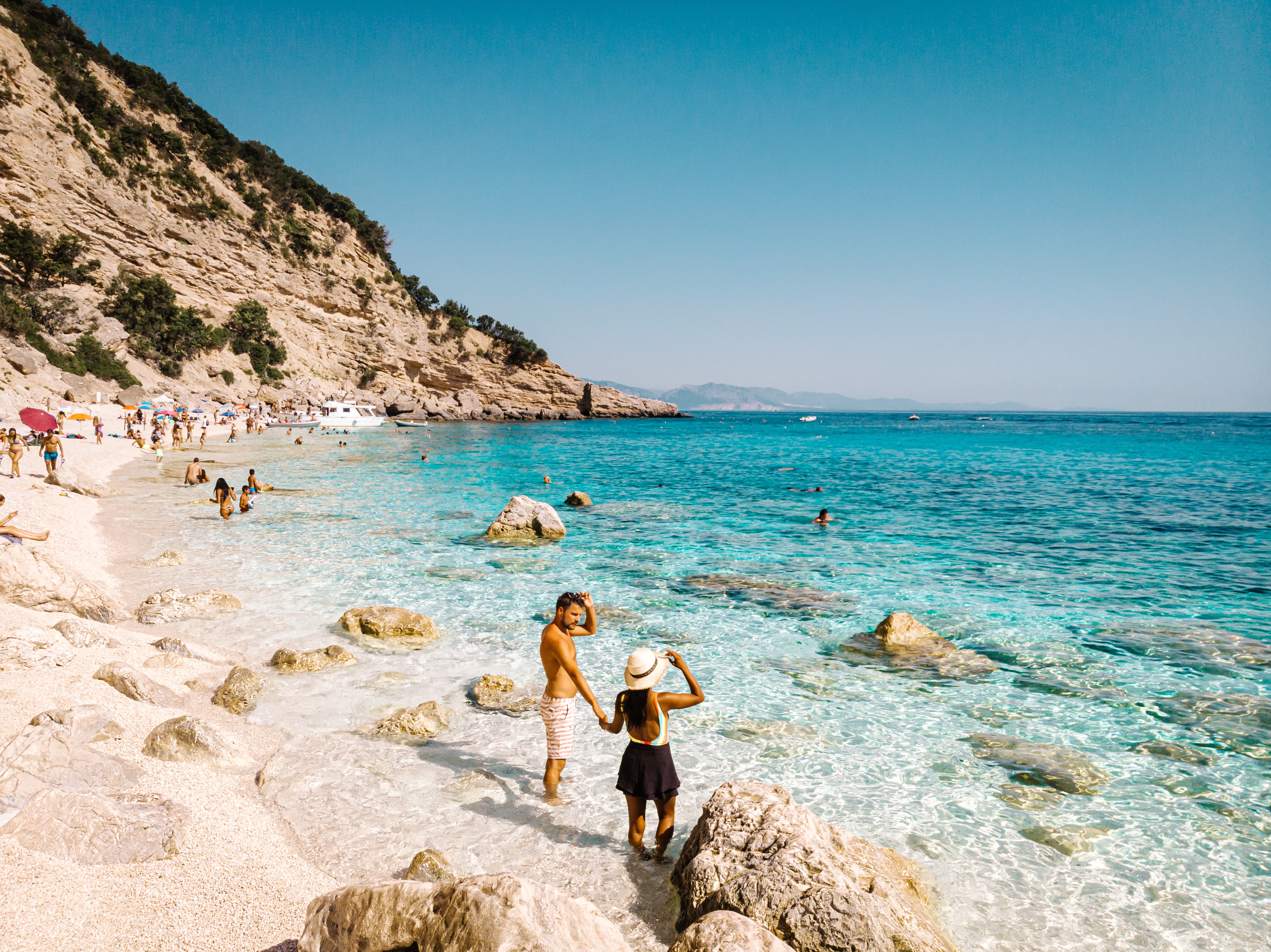 a couple stands in blue water looking out over rocks